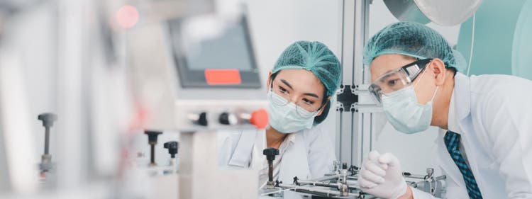 Both male and female Asian scientists are outfitted with protective gear. Examining the factory's machinery and materials used in the mask-making process. Covid 19 is a piece of preventive equipment.