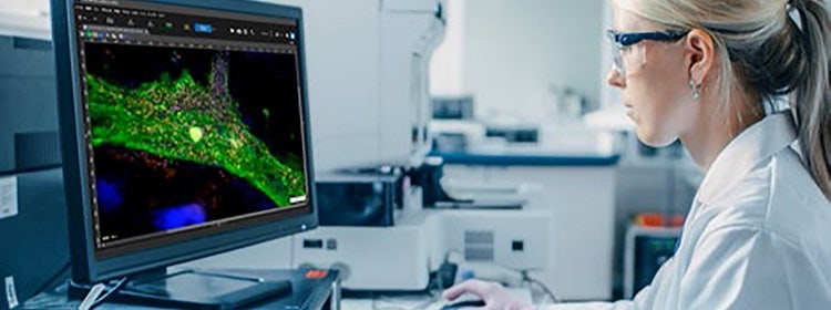 Woman sitting in front of an Olympus microscope looking at a sample on a computer monitor