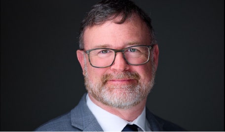 A person wearing glasses and a suit AI-generated content may be incorrect.