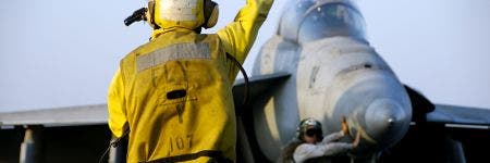 Controlador aéreo dirigiendo un avión de combate F-18 Hornet por la cubierta de vuelo de un portaaviones