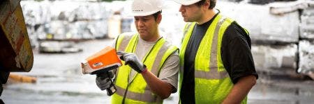 Trabajadores de la industria del reciclaje usando un analizador XRF para clasificar el metal en un depósito de chatarra