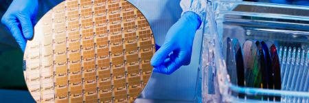 Wafer semiconduttore tenuto da un tecnico in tuta da lavoro e guanti sterili in un impianto produttivo