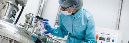 Pharmaceutical plant worker inspecting a gauge on a medicine processing tank as part of drug manufacturing process